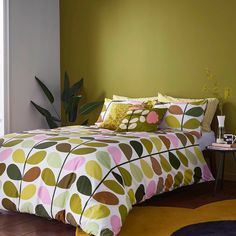 a bed in a room with green walls and colorful comforter on top of it