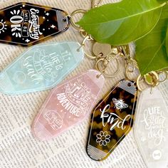 four keychains with different designs on them sitting next to a green leaf and newspaper