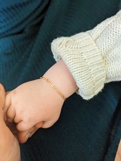 a person holding a baby's hand while wearing a white knitted sweater and gold chain bracelet