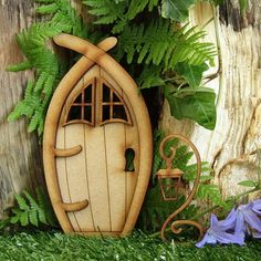 an image of a wooden fairy door in the grass with flowers and plants around it