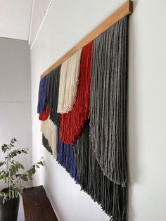 a wall hanging with fringes on it next to a potted plant in a room