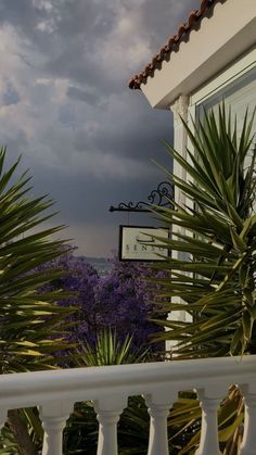 a sign on the side of a building with palm trees in the foreground and clouds in the background