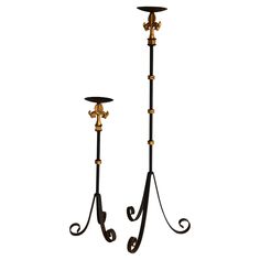 two black and gold metal candlesticks with handles on each side, one holding a candle