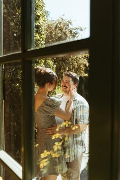 a man and woman standing next to each other in front of a window with trees outside