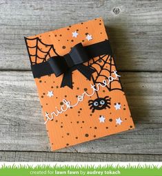 an orange halloween card with a black bow and spider web on it, sitting on a wooden surface