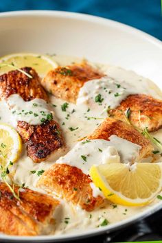 a white plate topped with fish covered in sauce and lemon wedges