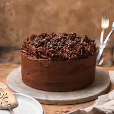 a chocolate cake sitting on top of a white plate next to a knife and fork