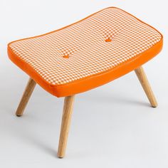 an orange foot stool sitting on top of a wooden leg rest with holes in it