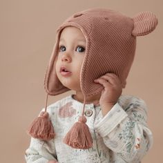 a small child wearing a knitted hat with tassels and holding a pine cone