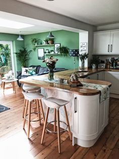 a kitchen with green walls and wooden flooring is pictured in this image, there are stools at the center of the island