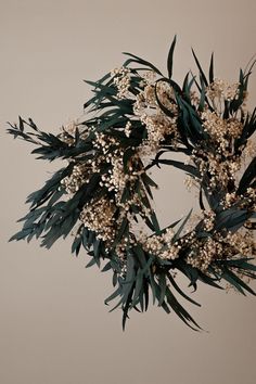 a wreath with white flowers and green leaves hanging from the ceiling in front of a wall