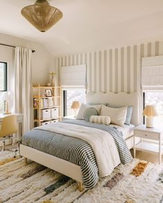 a bedroom with striped walls and white bedding, rugs on the floor, two lamps hanging from the ceiling