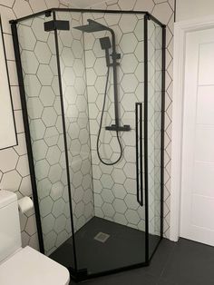 a black and white bathroom with hexagonal tiles on the wall, shower head, and toilet