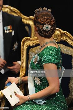 a woman in a green dress is sitting on a gold chair and wearing a tiara