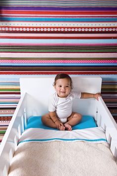 a baby sitting on top of a bed in front of colorful striped wallpapers