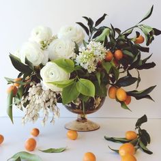 a vase filled with white flowers and greenery on top of a table next to an orange