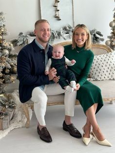 a man and woman sitting on a bench with a baby in front of christmas trees