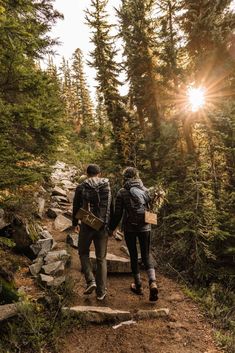 two people walking up a trail in the woods with backpacks on their back,