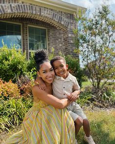 a young boy and girl hugging each other in front of a brick house with green grass