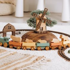 a wooden toy train set on a white rug with a windmill in the background and other toys