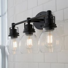 a bathroom light fixture with five clear globes hanging from it's arm in front of a white brick wall