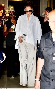 a woman in white shirt and grey pants walking into a building with other people behind her