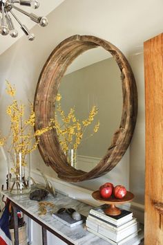 a round mirror sitting on top of a wooden shelf next to a vase filled with flowers