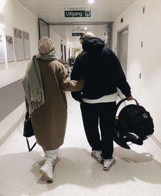 two people walking down a hallway with luggage in their hands and one person wearing a hoodie