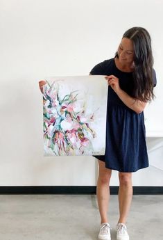 a woman is holding up a large painting