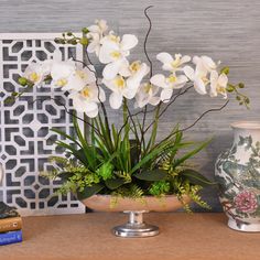 some white flowers are in a bowl on a table next to books and a vase