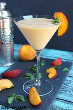 a drink in a martini glass garnished with peaches on a slate tray