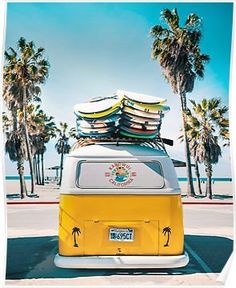 a yellow and white vw bus with surfboards stacked on top in front of palm trees