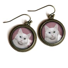 Purrfect earrings for the cat lover in your life.  An original illustration of a fluffy white cat cat set under glass, then placed into a simple brass setting. We prefer the look of our nickel free brass ear wires with these earrings, but those with sensitive skin can update to surgical steel for a small charge. . Earring clips may be available in place of wires.  Please ask before ordering if you would prefer clip-ons. Decoupage Glass, Cabochon Earrings, Russian Blue Cat, Cat Person, Cat Earrings, Cat Illustration, Light Weight Earrings, Sweet Treat, White Cat