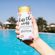 a person holding up a can of beer near a swimming pool with palm trees in the background