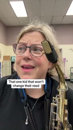 a woman with glasses holding a saxophone up to her face in an office setting that says, that's kid thrown it changes their reeds