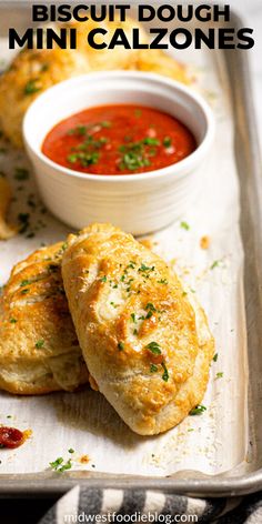 two biscuits on a baking sheet with a bowl of tomato soup in the background and text overlay reading biscuit dough mini calzonees