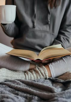 an open book sitting on top of a table next to a cup of coffee and a blanket