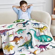 a little boy sitting on a couch under a blanket with dinosaurs all over it