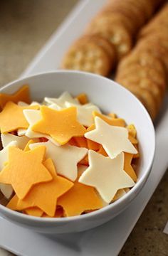 a white bowl filled with cheese and star shaped cookies next to crackers on a table