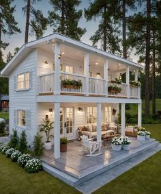 a white house with lots of windows and plants on the front porch, surrounded by trees