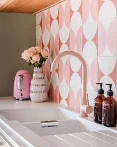 a kitchen sink with soap dispensers and pink flowers on the counter top