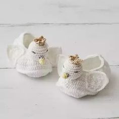 two white crocheted baby shoes with gold bows on them sitting on a white wooden surface