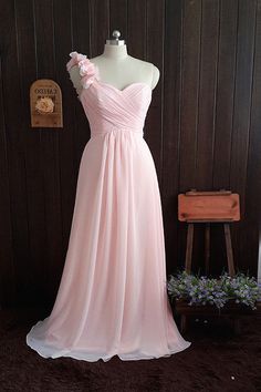 a pink dress is on display in front of a wooden wall and purple flowers are behind the mannequin