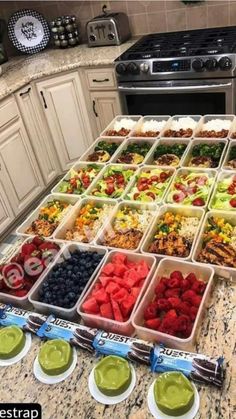 a kitchen counter filled with trays of fruit and veggies next to an oven