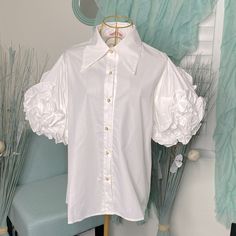 a white shirt with ruffles is hanging on a hanger in front of a blue chair