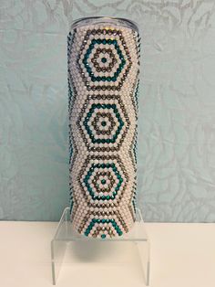 a beaded vase sitting on top of a white table next to a blue wall