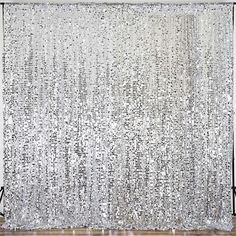 a white curtain with silver sequins hanging from it's side in front of a wooden floor