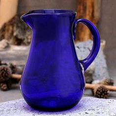 a blue glass pitcher sitting on top of a stone slab next to pine cones and branches