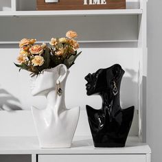 two black and white vases with flowers in them on a shelf next to a clock