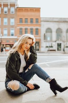 a woman sitting on the ground with her legs crossed and looking at the camera while wearing black boots